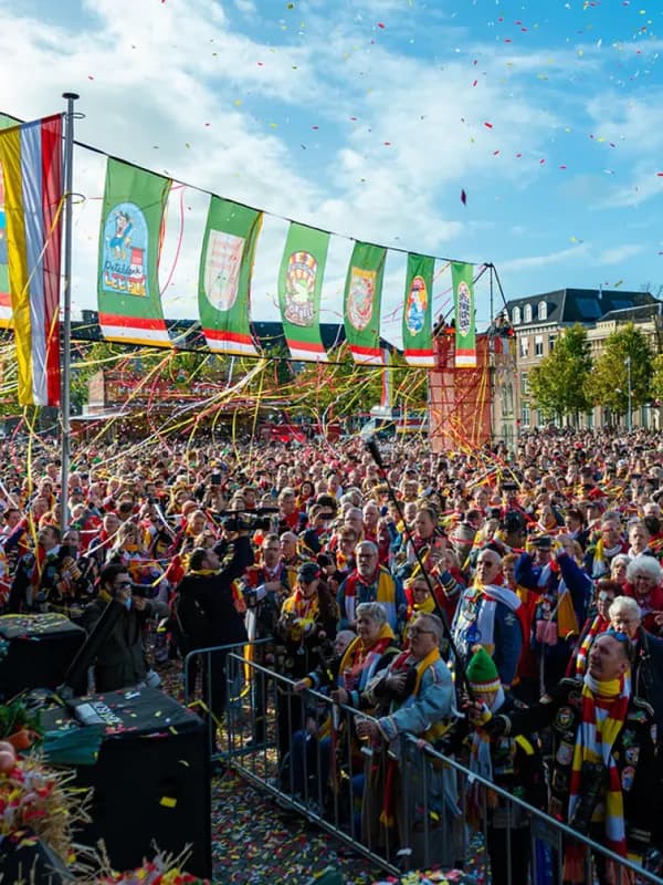 Feestende menigte bij het podium op de markt van Oeteldonk met vaandels, confetti en slingers